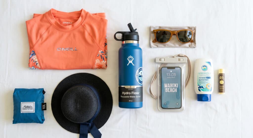 Waikiki packing checklist flat-lay showing mineral sunscreen, rash guard, waterproof phone pouch, and beach essentials for a Hawaii trip